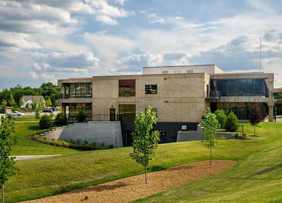 A modern building with a flat roof and large windows is surrounded by a grassy area with trees.