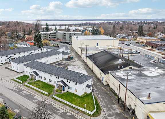 A large white building with a black roof is surrounded by other buildings and trees.