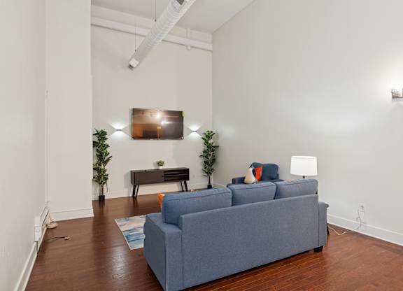 A grey couch sits in a white room with a wooden floor and a white wall.