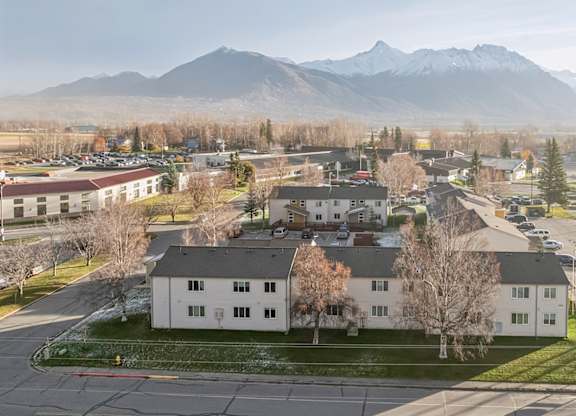A large white building sits in the middle of a parking lot with mountains in the background.
