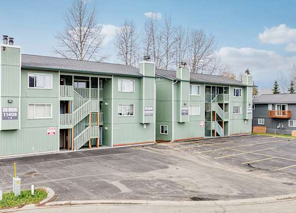 A large green building with a parking lot in front.