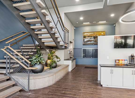 A staircase with a metal railing and wooden steps leads to a brightly lit room with a kitchen area.