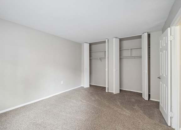 A bedroom with white walls and a carpeted floor with a white door on the right.