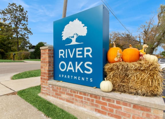 the sign for river oaks apartments in front of a brick wall with pumpkins at River Oaks, North Aurora, 60542