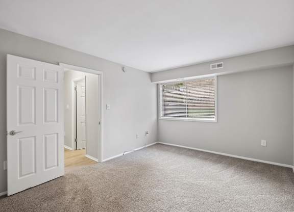 A bedroom with a white door and a window with blinds.