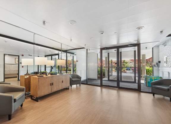 A spacious waiting room with a grey sofa, wooden cabinet, and glass doors leading to the outside.