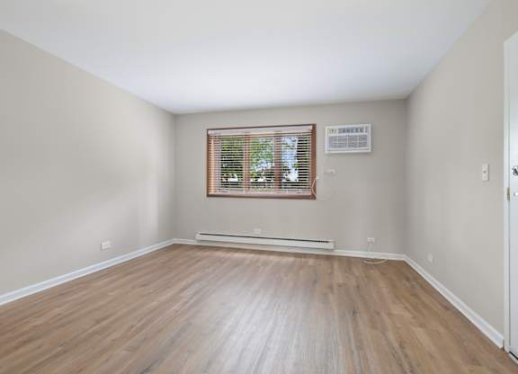 A room with wooden flooring and a window with blinds.
