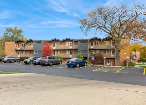 an apartment complex with cars parked in a parking lot at River Oaks, North Aurora, 60542