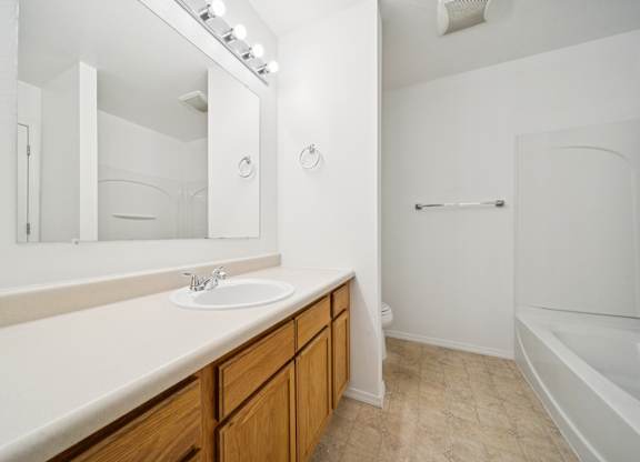 A white bathroom with a sink, mirror, and bathtub.