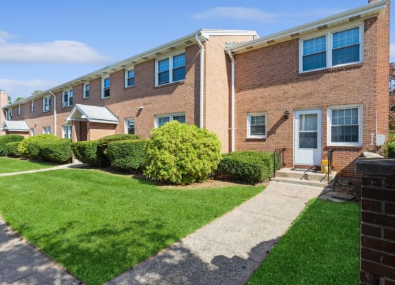 the front of a brick apartment building with a sidewalk and grass