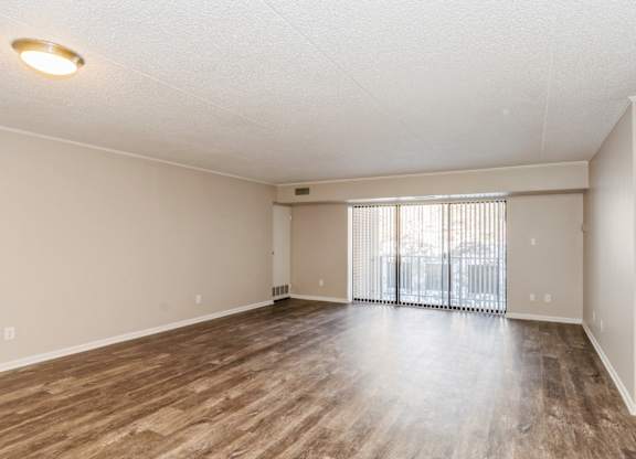 A spacious room with wooden flooring and a sliding glass door.