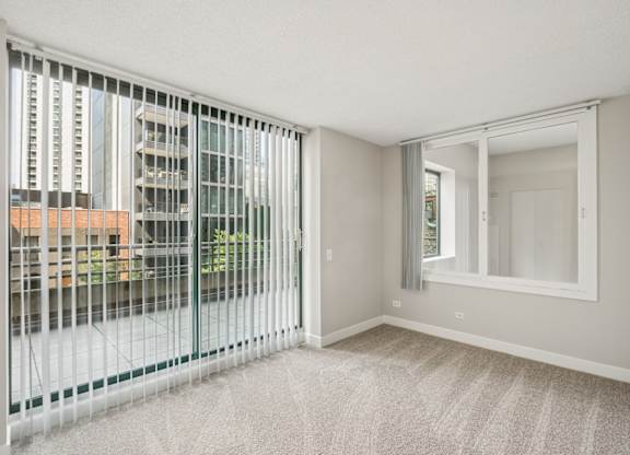 A room with a carpeted floor and a large window with a view of a cityscape.