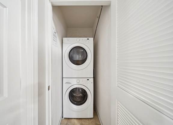 A white washing machine and dryer in a small, white-walled laundry room.