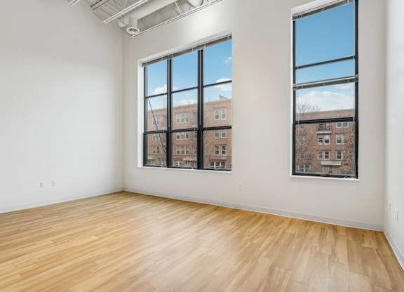 A room with wooden floors and two windows showing a view of a building.