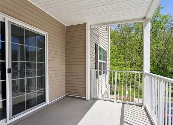 A screened porch with a white railing and a view of trees.