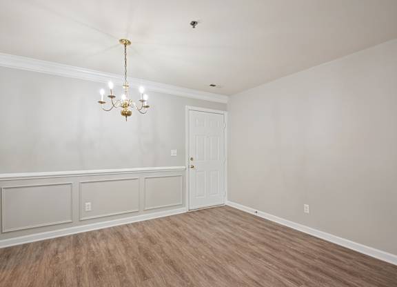A room with a chandelier, a door, and a wall with paneling.