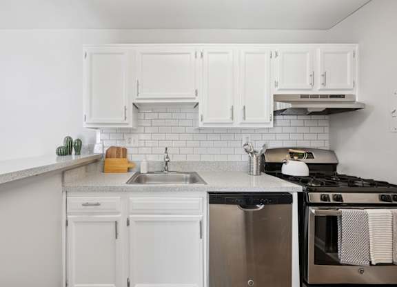 A white kitchen with a stove, sink, and cabinets.