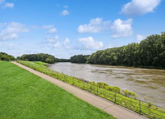 A river flows through a green landscape with a fence alongside a walkway.