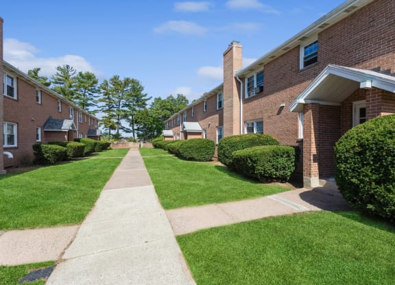 a sidewalk in front of the apartment building with green grass and bushes