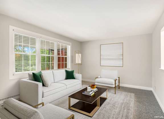 A living room with a white couch, a coffee table, and a window with blinds.