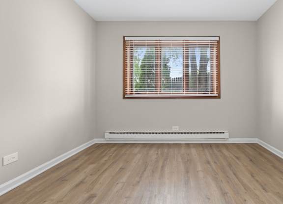 A room with a window and a radiator on a wooden floor.