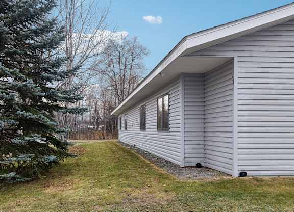 A house with a grey siding and a tree in front of it.