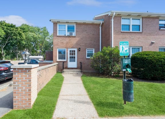 the front of a brick apartment with a sidewalk and a doggy trash station