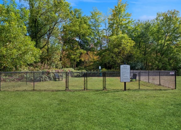 a dog park with a fence and a sign in the grass with the rules at Arbor Commons