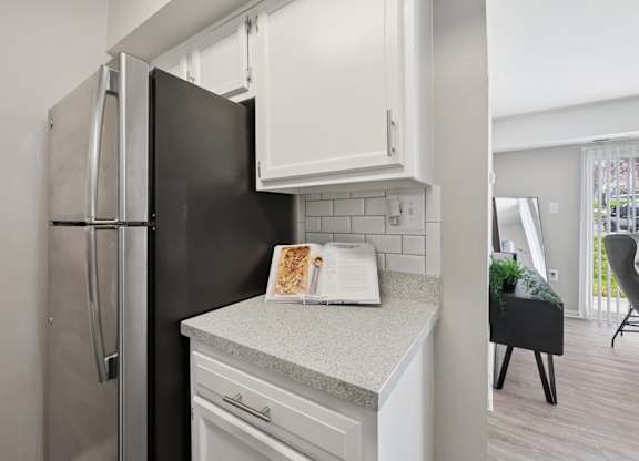 A black refrigerator is in a kitchen with white cabinets and a countertop.