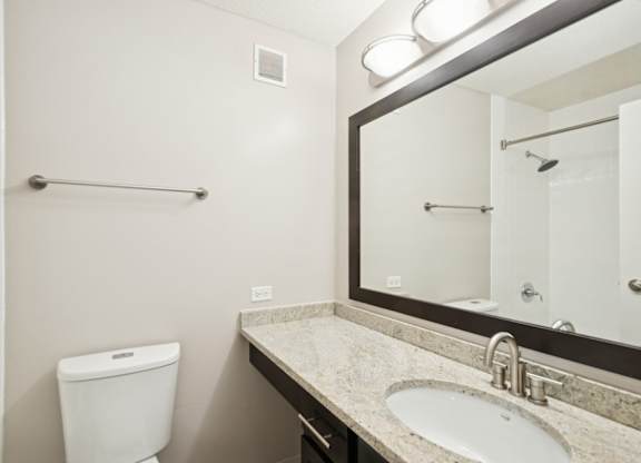 A bathroom with a toilet, sink, mirror and towel rack.