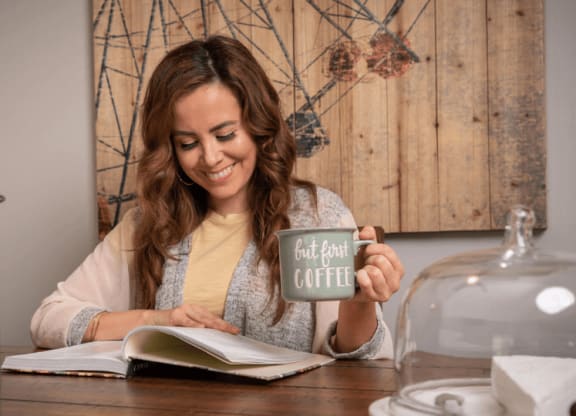 a woman sitting at a table with a book and a mug  at The Township at St. Charles, St. Charles, IL