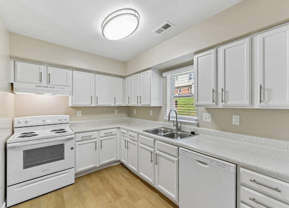 A white kitchen with a stove, sink, and cabinets.
