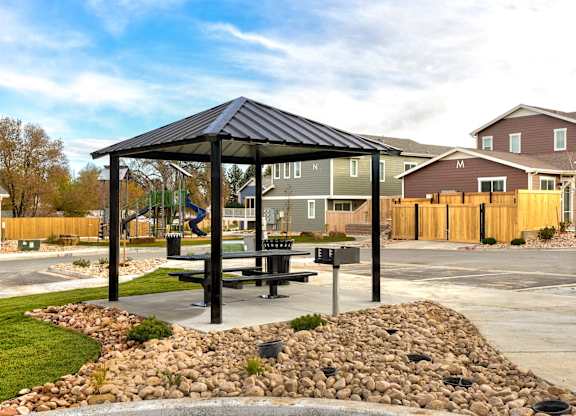 A black gazebo with a table and chairs is surrounded by a rock garden.