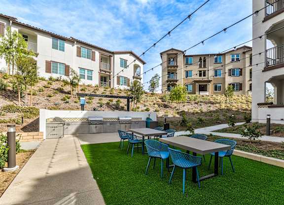 A patio with blue chairs and a table is in front of apartment buildings.