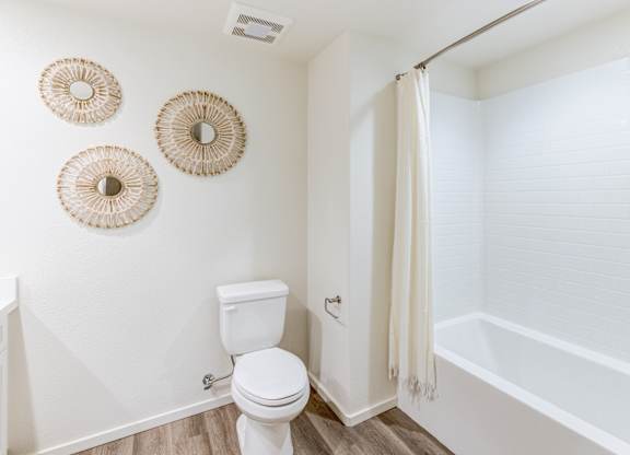 A white toilet sits in a bathroom with three wall hangings.