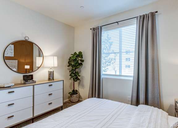 A bedroom with a large bed, a mirror, and a potted plant.