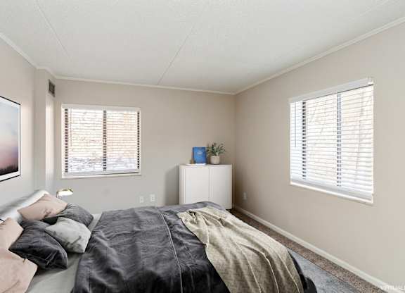 A bedroom with a bed, a nightstand, and a window with blinds.