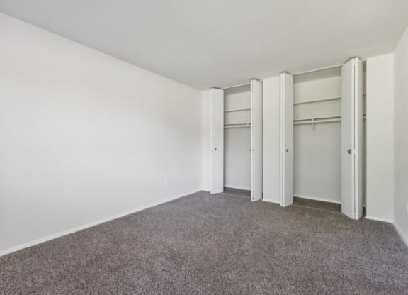 an empty room with white walls and carpet and closet doors at Briarwood Apartments, Dumfries, VA