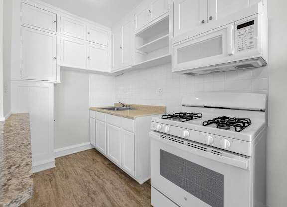 A white kitchen with a stove, microwave, and cabinets at Pleasant Oak Apartments, Oak Park, Illinois