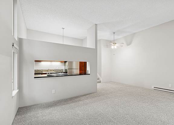 A spacious room with a carpeted floor and a window with a view of a kitchen.