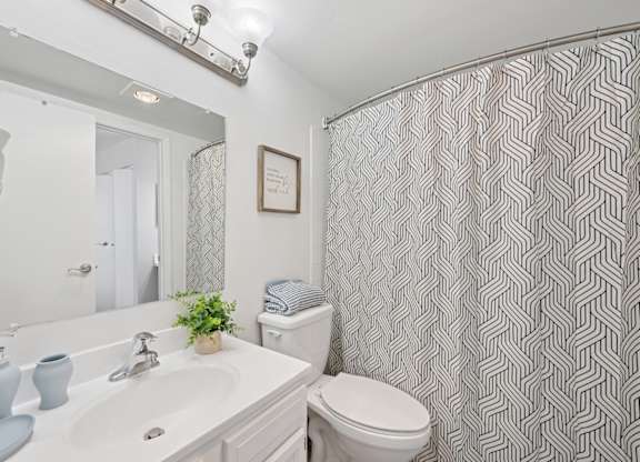 A bathroom with a white sink, toilet, and a grey and white shower curtain.
