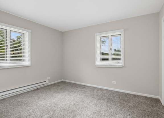A room with a carpeted floor and two windows with blinds.