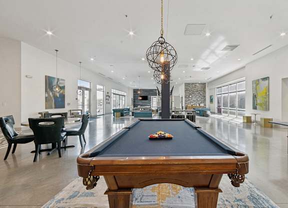 A pool table is in the middle of a room with a black chair and a chandelier.