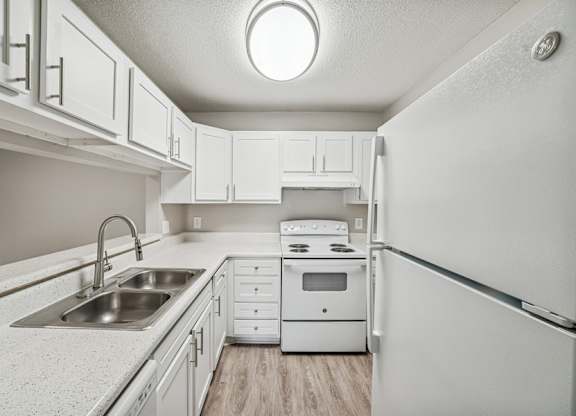 A white kitchen with a sink, stove, and refrigerator.