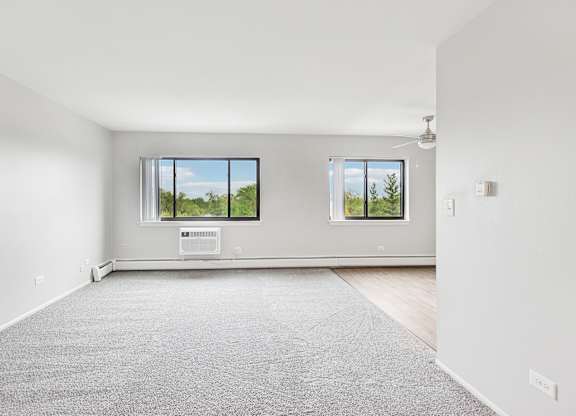 A large livingroom with a grey carpet and two windows.