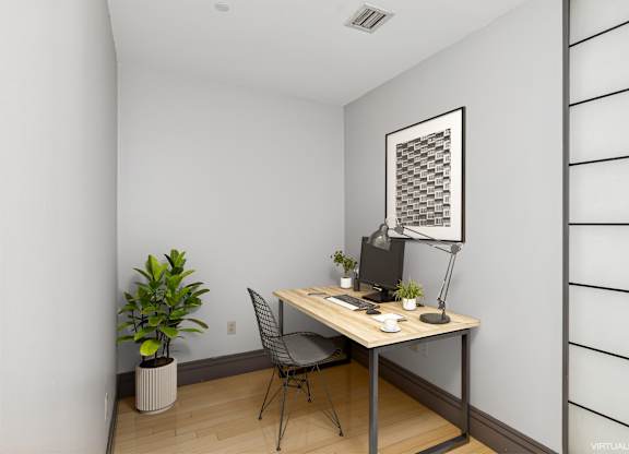 A room with a desk, chair, and a potted plant.
