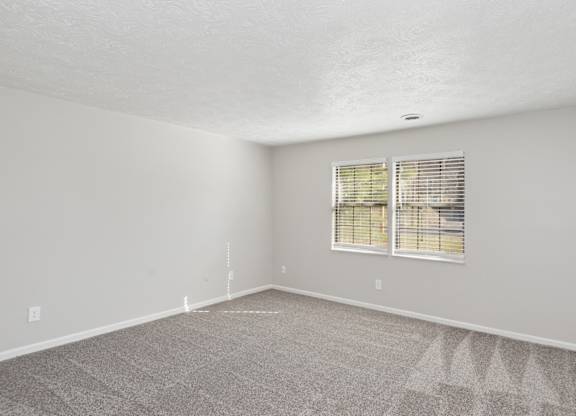 A room with a carpeted floor and a window with blinds.