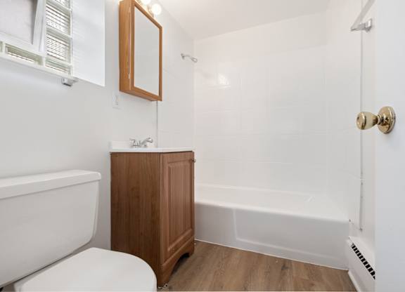 A white bathroom with a wooden cabinet and a white tub.
