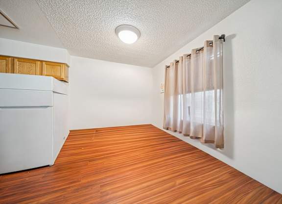 A room with wooden flooring and a white refrigerator.