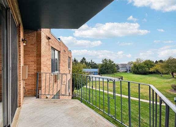 A balcony with a metal railing overlooks a green lawn.